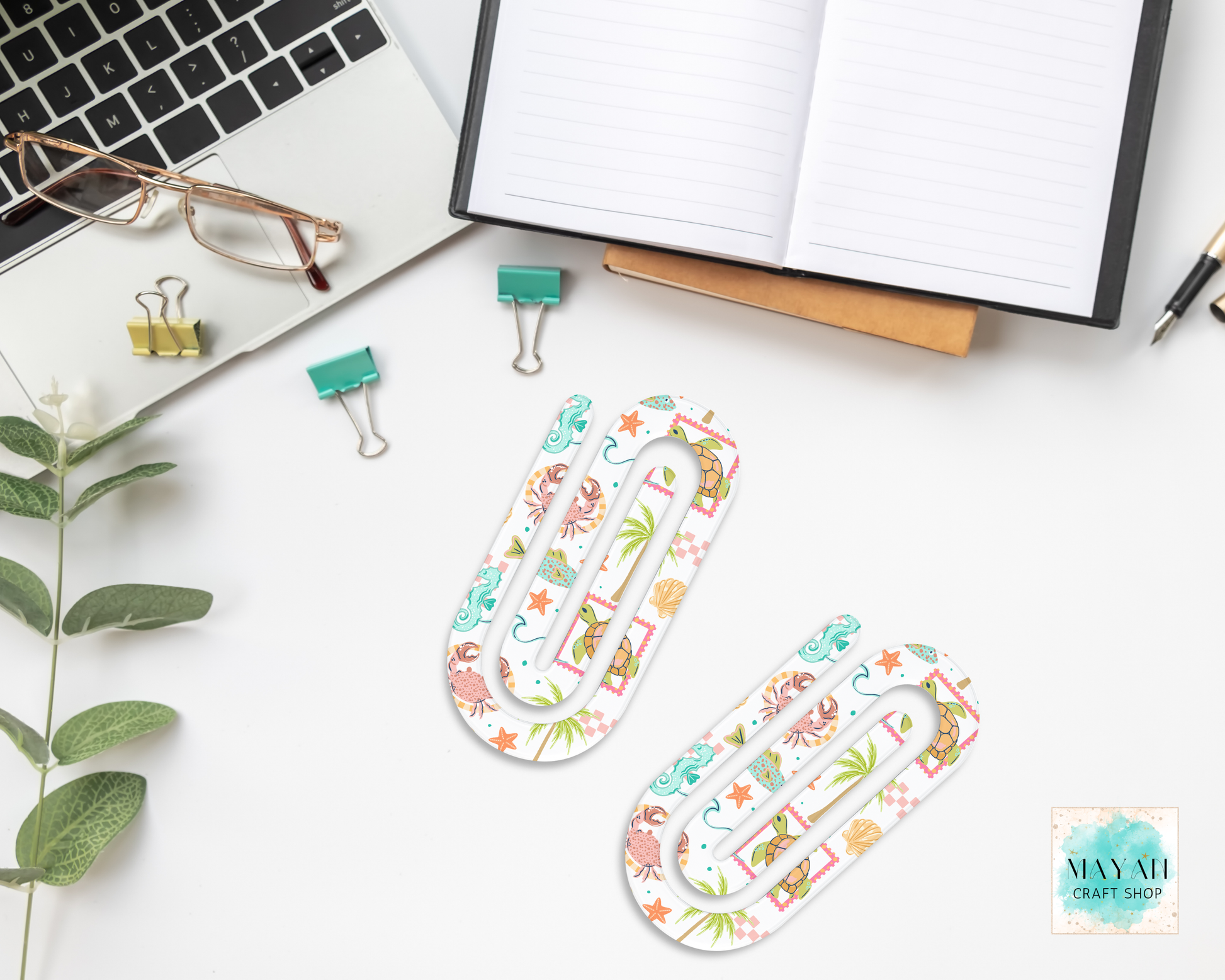 Decorative paper clips on a desk with office supplies and a laptop.