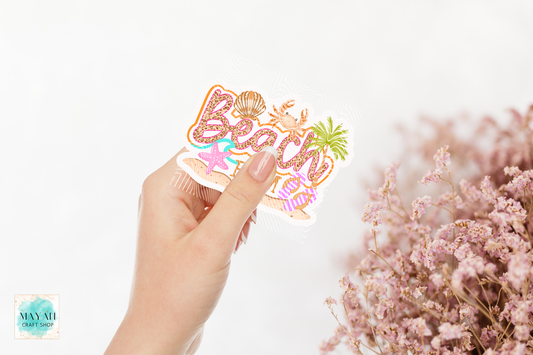 Hand holding a 'Beach Time' sticker with floral designs on a light background