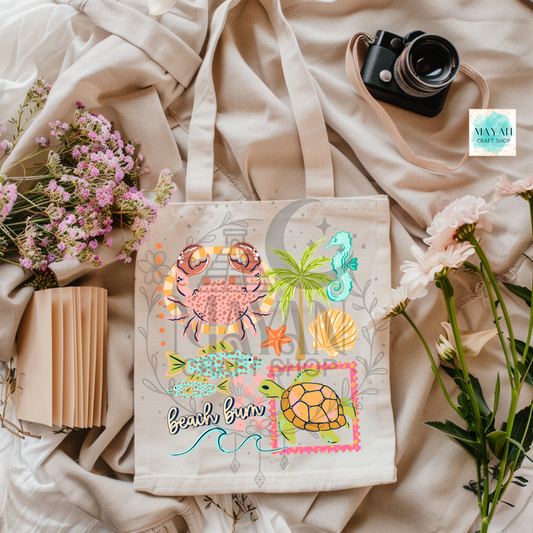 Beige tote bag with beach-themed design featuring a turtle, palm tree, and seashells on a light fabric background.