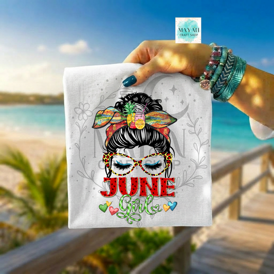 Hand holding a towel with 'June Girl' design against a beach background
