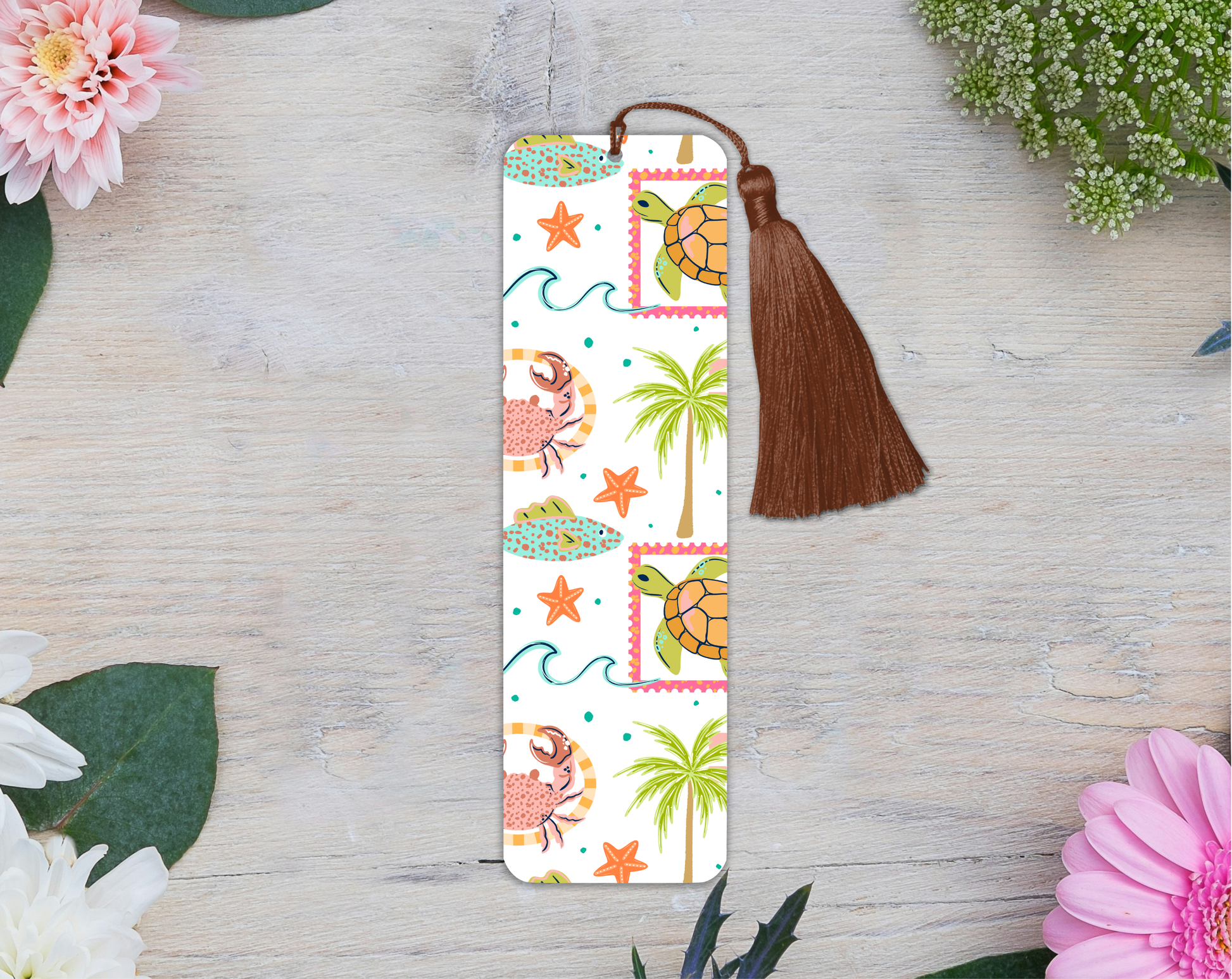Bookmark with tropical design featuring turtles, palm trees, and flowers on a wooden surface with flowers around.