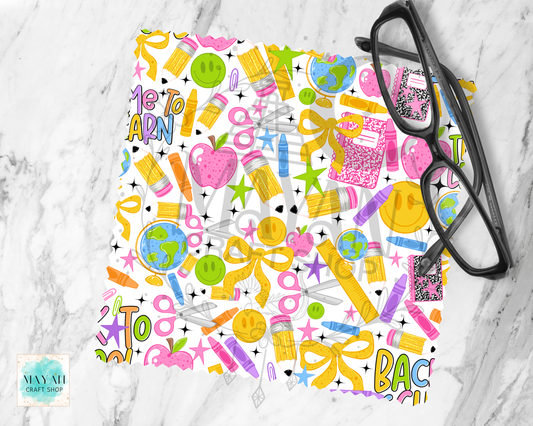 A square piece of lens cloth cleaner with a colorful 'Back to School' pattern, styled flat-lay on a white marble background with black eyeglasses.