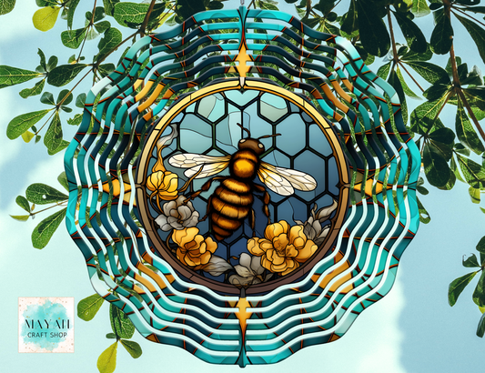 Decorative wind spinner with a bee and floral design, surrounded by green leaves.