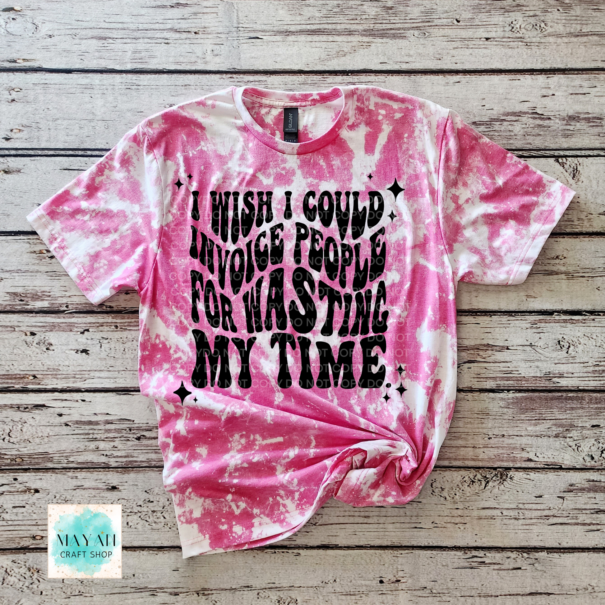 Pink tie-dye t-shirt with black text on a wooden surface, featuring the brand 'Mayan Craft Shop'.