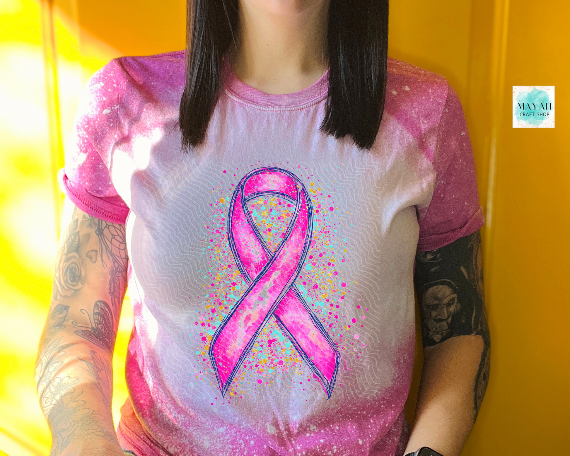 Person wearing a shirt with a pink ribbon design against a yellow background