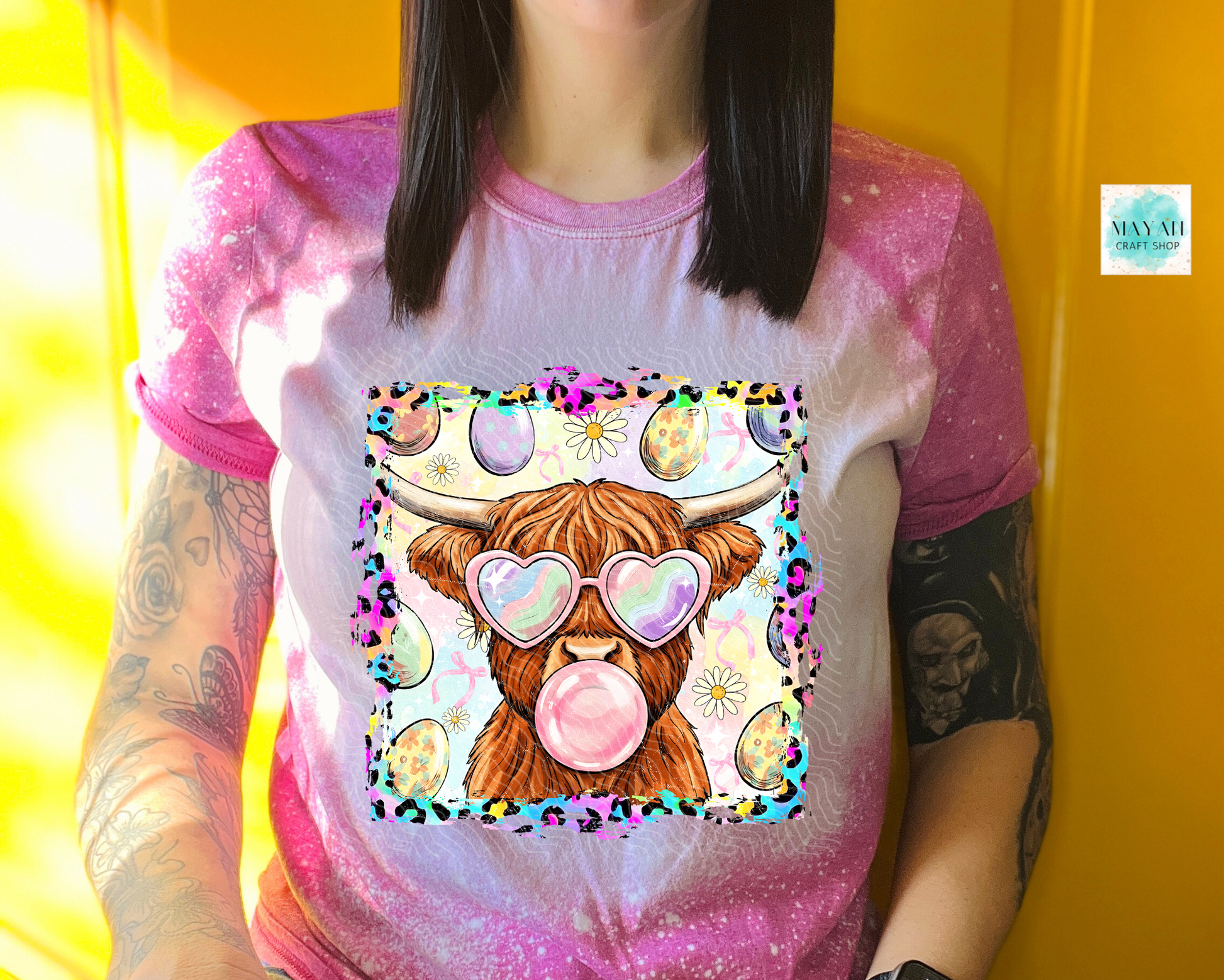 Person wearing a t-shirt with a colorful design of a cow blowing a bubble gum bubble, set against a yellow background.