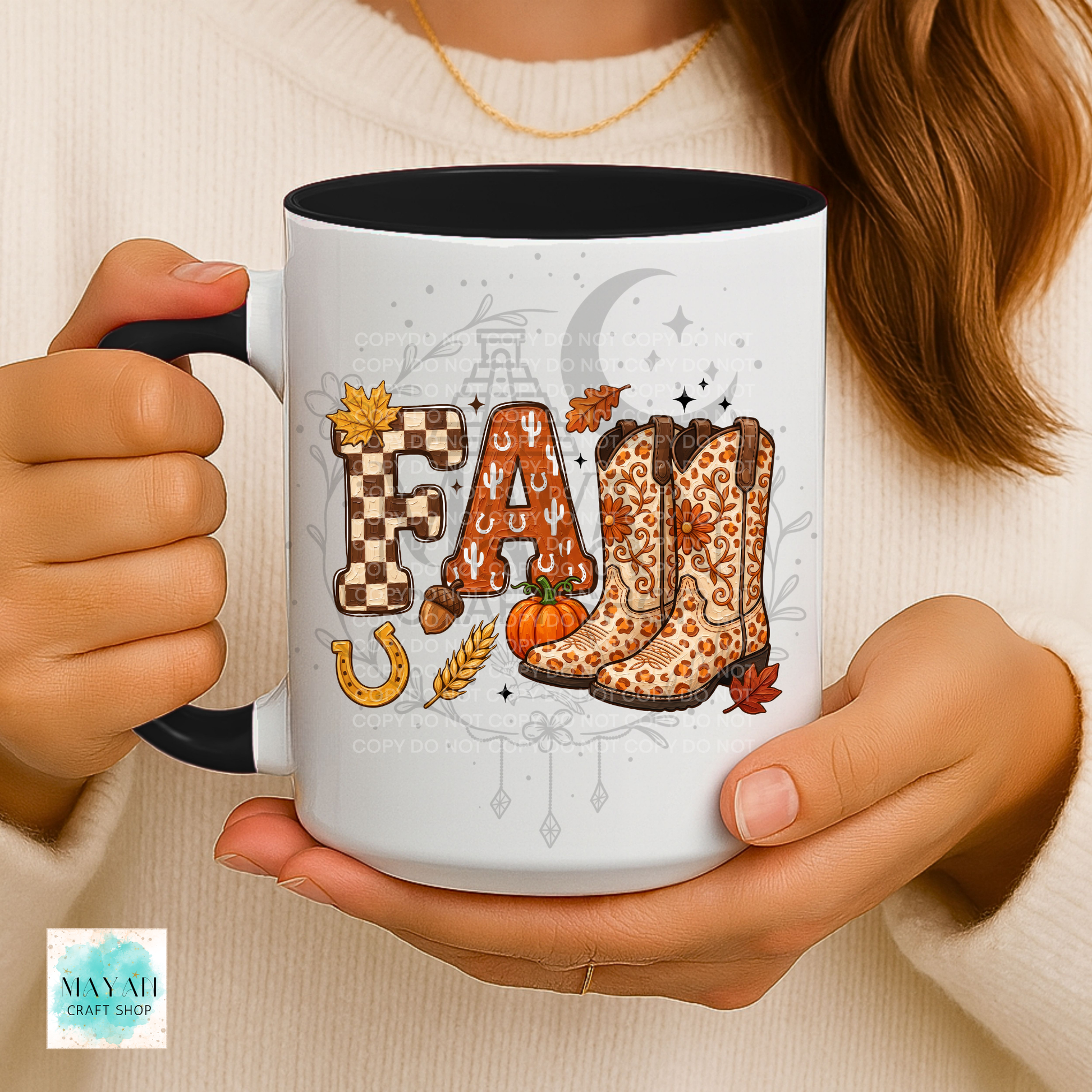 A person holds a white ceramic mug with a black handle and interior. The mug features a fall-themed graphic spelling 'FALL' with checkered 'F', an 'A' made of horseshoes and acorns, leopard-print cowboy boots, a pumpkin, wheat, and autumn leaves.
