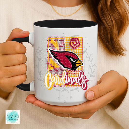 A person holding a white ceramic mug with a black handle and interior. The mug features a colorful football team logo and in a white script over a yellow, pink, and red patterned background.
