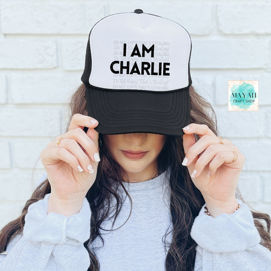 Person wearing a cap with 'I AM CHARLIE' text against a white brick wall.