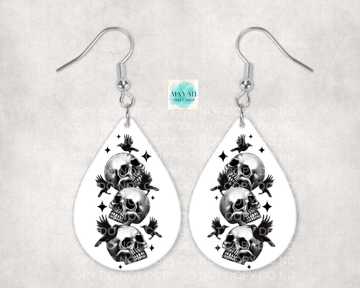 Teardrop-shaped earrings with skull and bird designs on a light gray background.