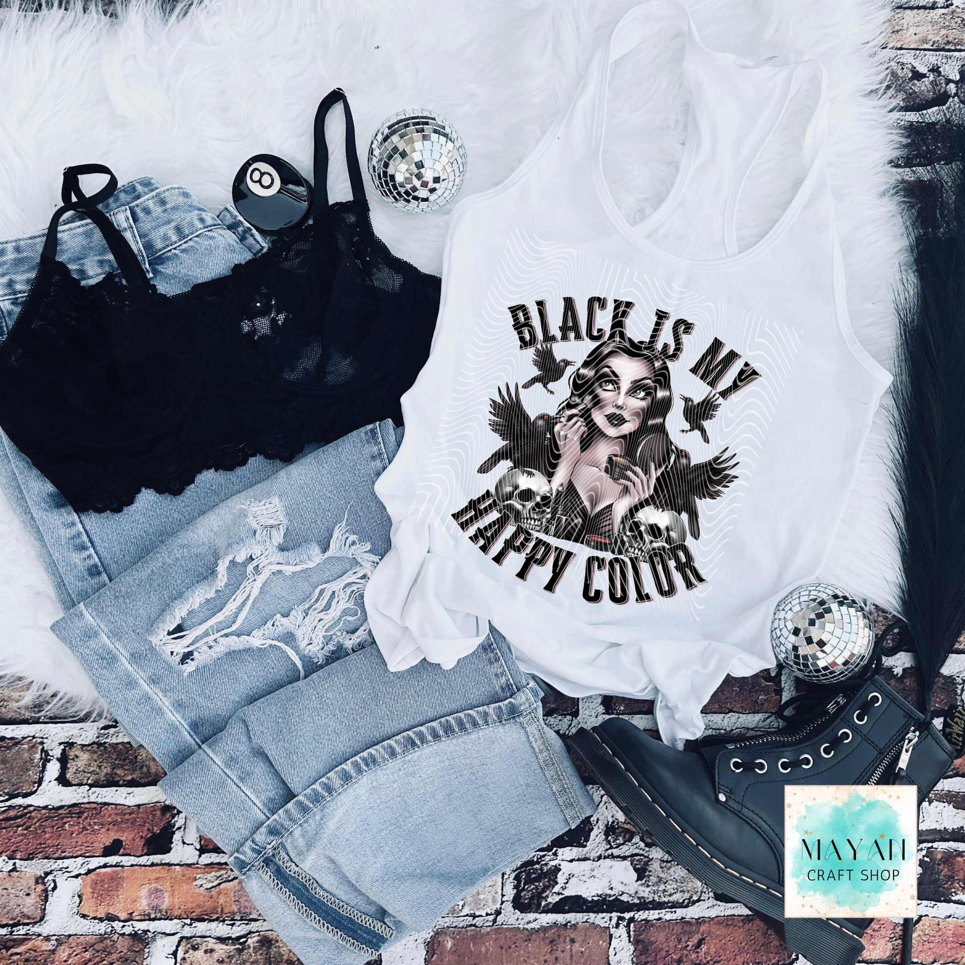 White tank top with graphic design and text, black bralette, denim shorts, and black high-heeled shoes on a brick surface.