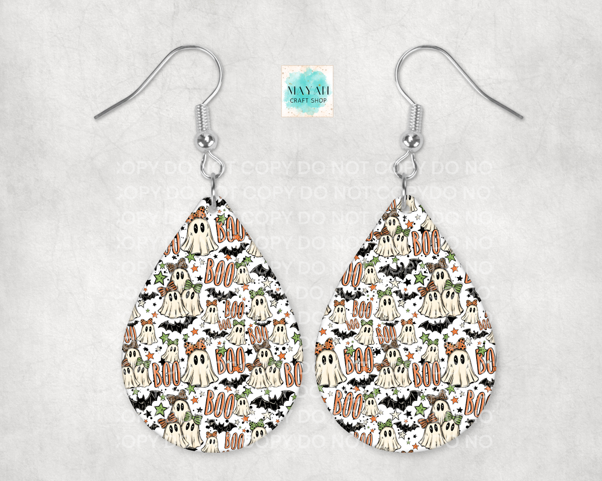 A pair of teardrop-shaped dangle earrings with a repeating Halloween pattern of ghosts, bats, and 'BOO' text, hanging from silver fishhook wires on a light gray textured background.