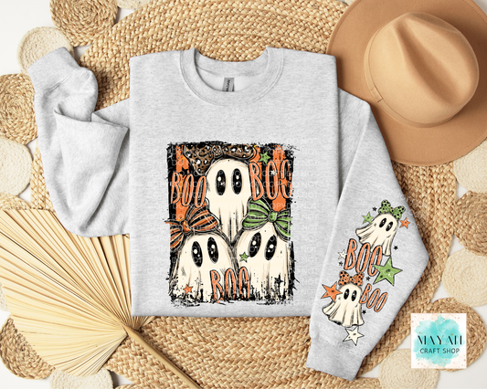A light gray long-sleeve crewneck sweatshirt with a Halloween graphic print featuring four ghosts and the words 'BOO'. The sweatshirt is displayed in a flat-lay arrangement on a woven mat with a tan hat, a paper fan.