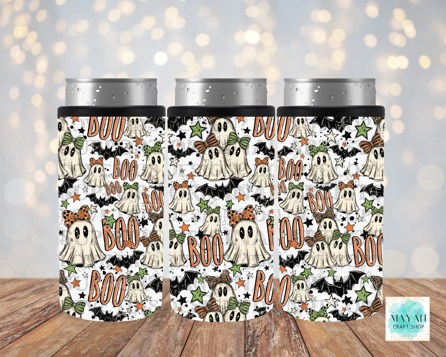 Three slim can coolers with a Halloween-themed pattern featuring cartoon ghosts, bats, stars, shown on a wooden surface with a soft bokeh light background.
