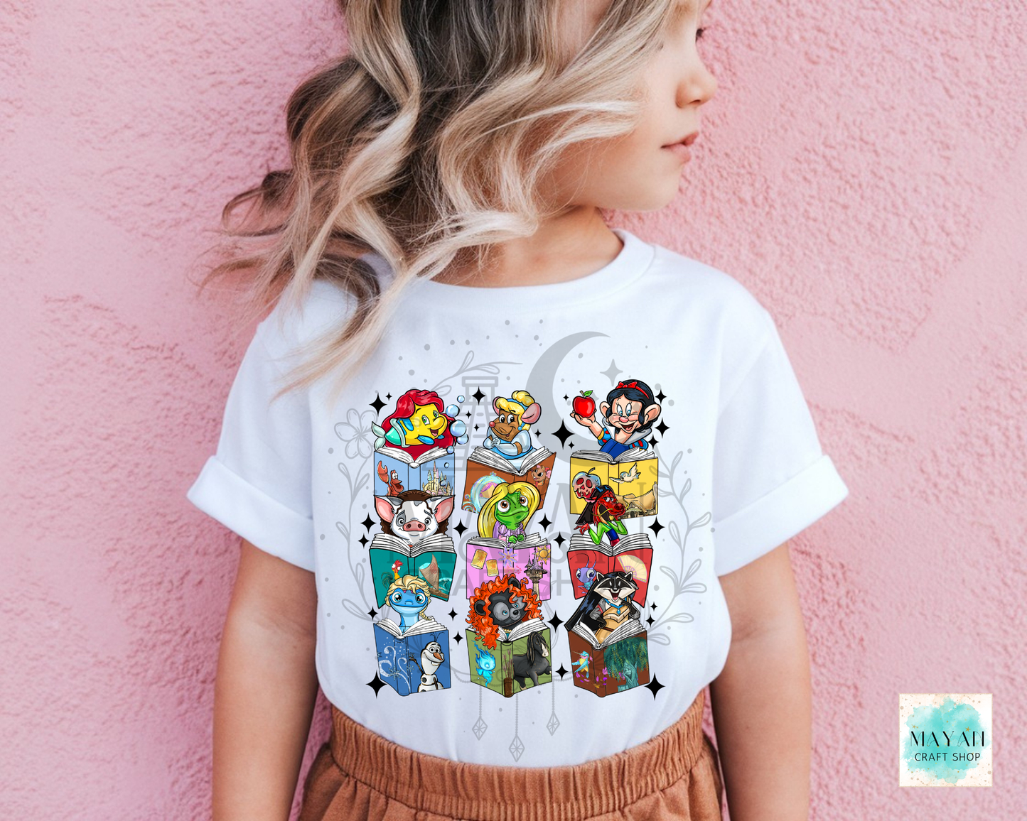 A child wearing a white graphic t-shirt featuring a colorful grid of cartoon books and characters, posed against a pink textured wall.