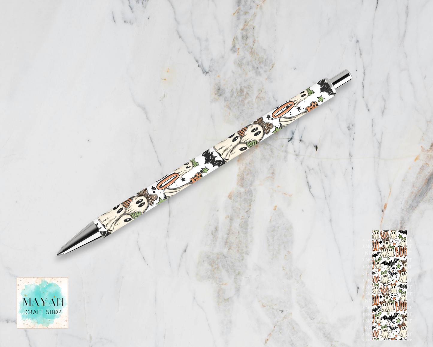 A retractable pen with a white barrel decorated with a repeating pattern of cartoon ghosts, pumpkins, and bats, resting diagonally on a white and gray marble background. A close-up of the pattern is shown in the bottom-right corner.