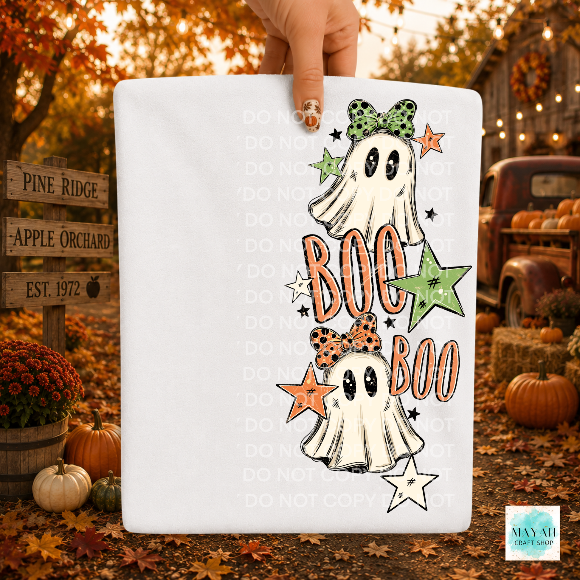 A white rectangular product held by a hand against an autumn outdoor backdrop with pumpkins, fall leaves, and a rustic truck. The product features a Halloween graphic with two cartoon ghosts, orange 'BOO' text, green and orange stars.