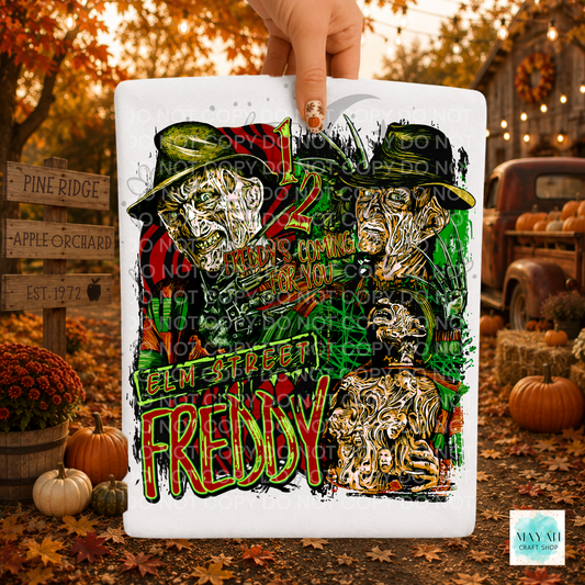 A hand holds a white shirt featuring a colorful graphic of two stylized Faces with a text. The background is a blurred autumn outdoor scene with pumpkins, fall leaves, and rustic decor.