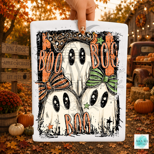 A hand holds a white shirt featuring a Halloween illustration of two ghosts with black eyes, orange and green bows, and the words 'BOO BOO BOO' and 'ROO ROO ROO' in orange. The background is a fall yard scene with pumpkins, autumn leaves, and rustic signs.
