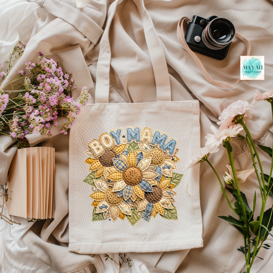 Tote bag with 'BOY MAMA' design on a soft fabric background with flowers and a camera.