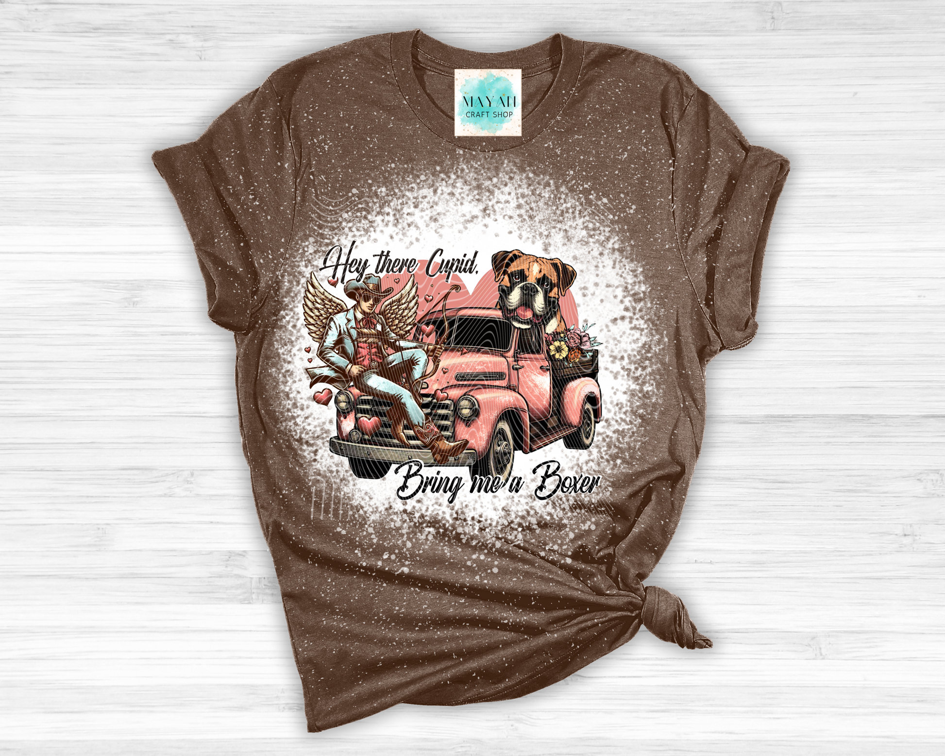 Brown t-shirt with graphic design of a dog, car, and angel on a white wooden surface