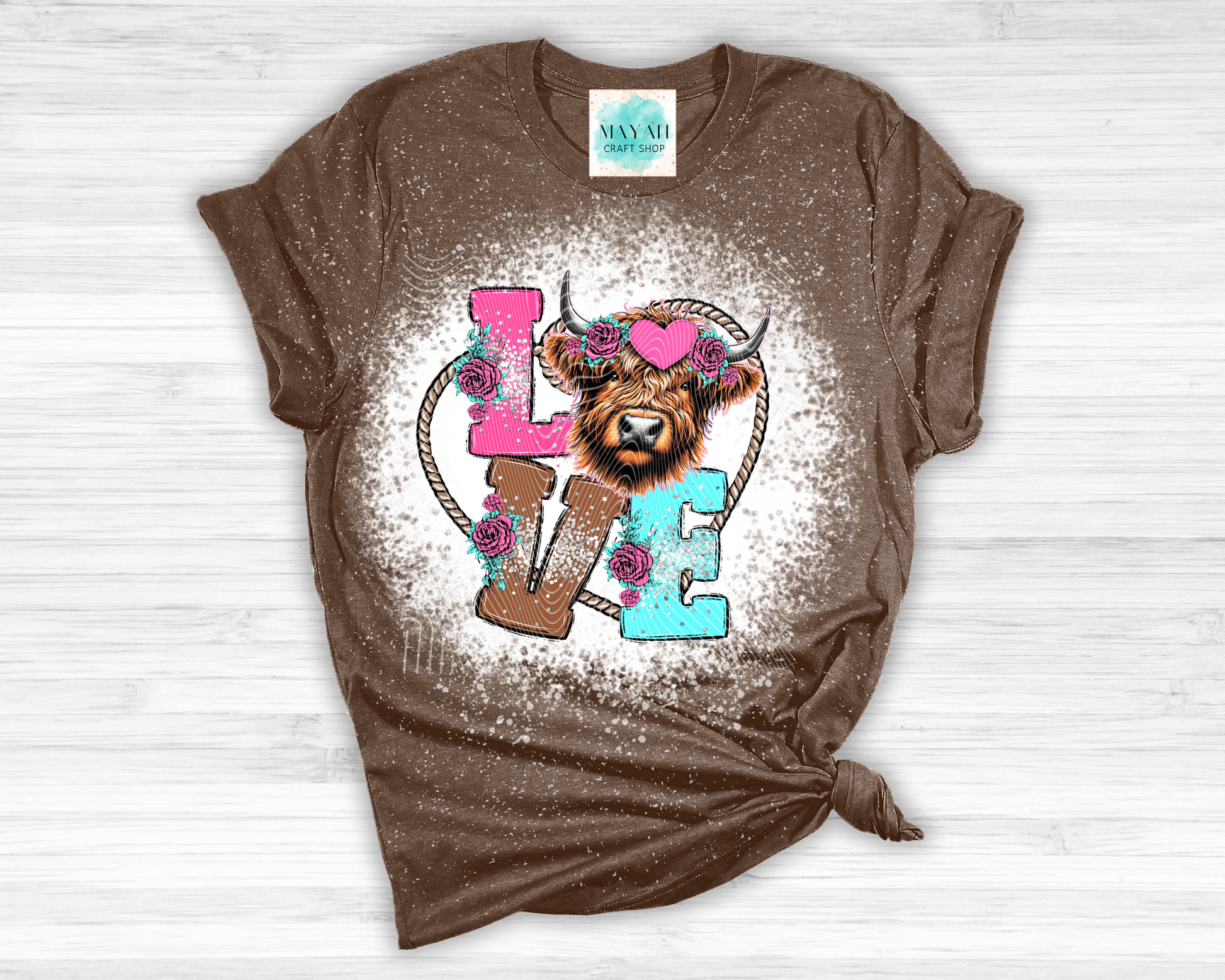 Brown t-shirt with a graphic design of a cow and 'LOVE' letters on a white wooden background