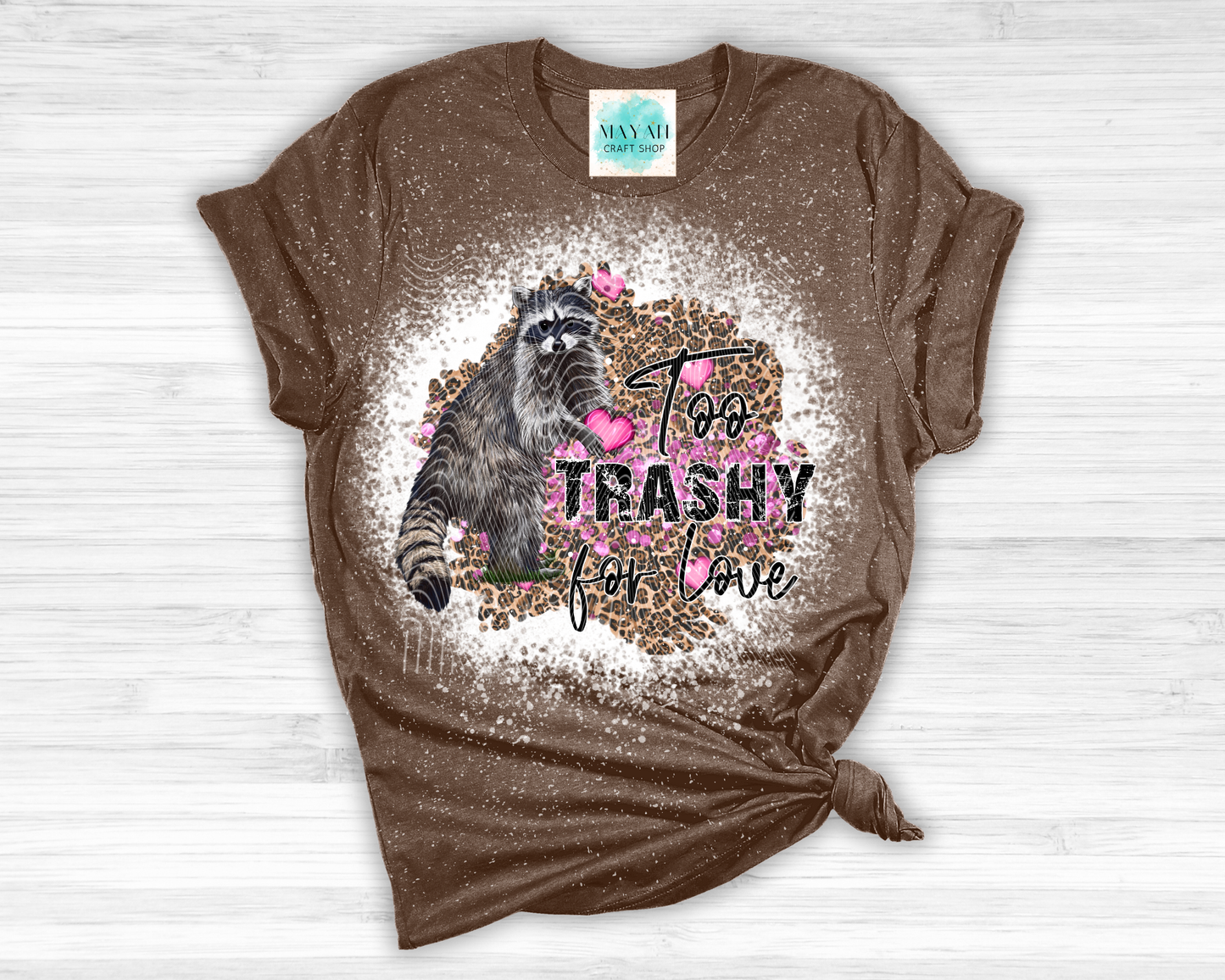 Brown t-shirt with a raccoon graphic and text on a white wooden surface