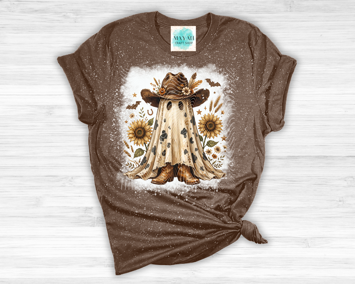 A brown short-sleeve t-shirt with a distressed texture, featuring a central graphic of a ghostly figure in a cowboy hat surrounded by sunflowers, laid flat on a white wood background.