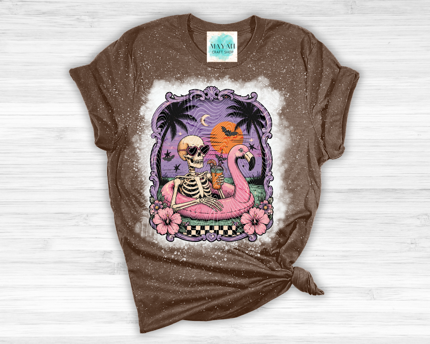 Brown t-shirt with a skeleton and flamingo design on a white wooden surface
