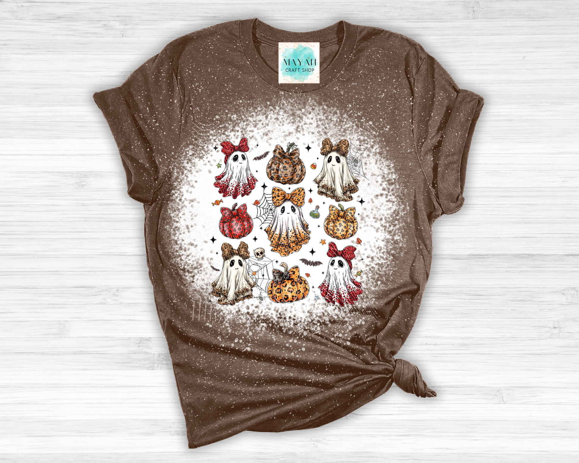 Brown t-shirt with a graphic design of ghosts and pumpkins on a white wooden surface