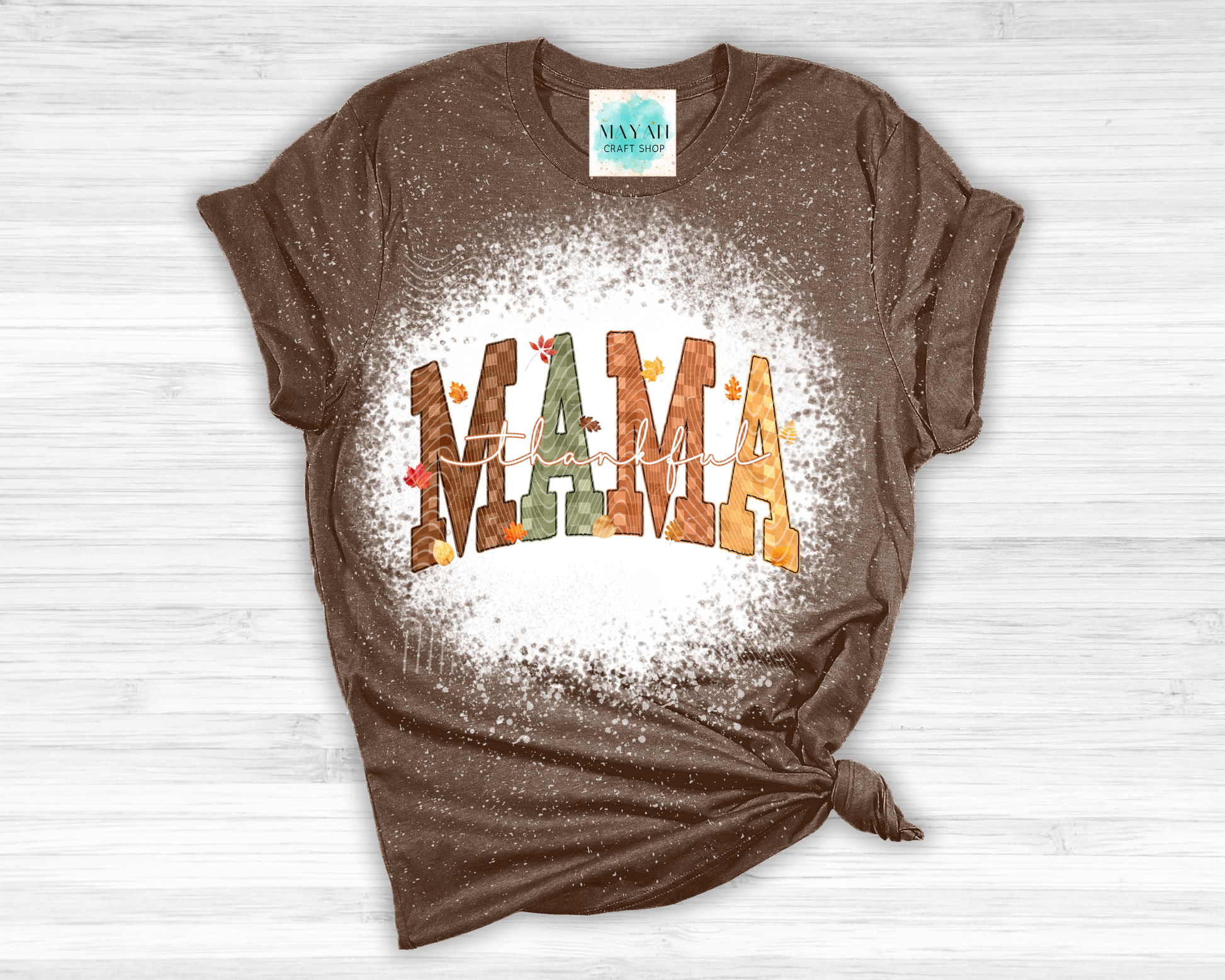 Brown t-shirt with 'MAMA' graphic on a white wooden surface