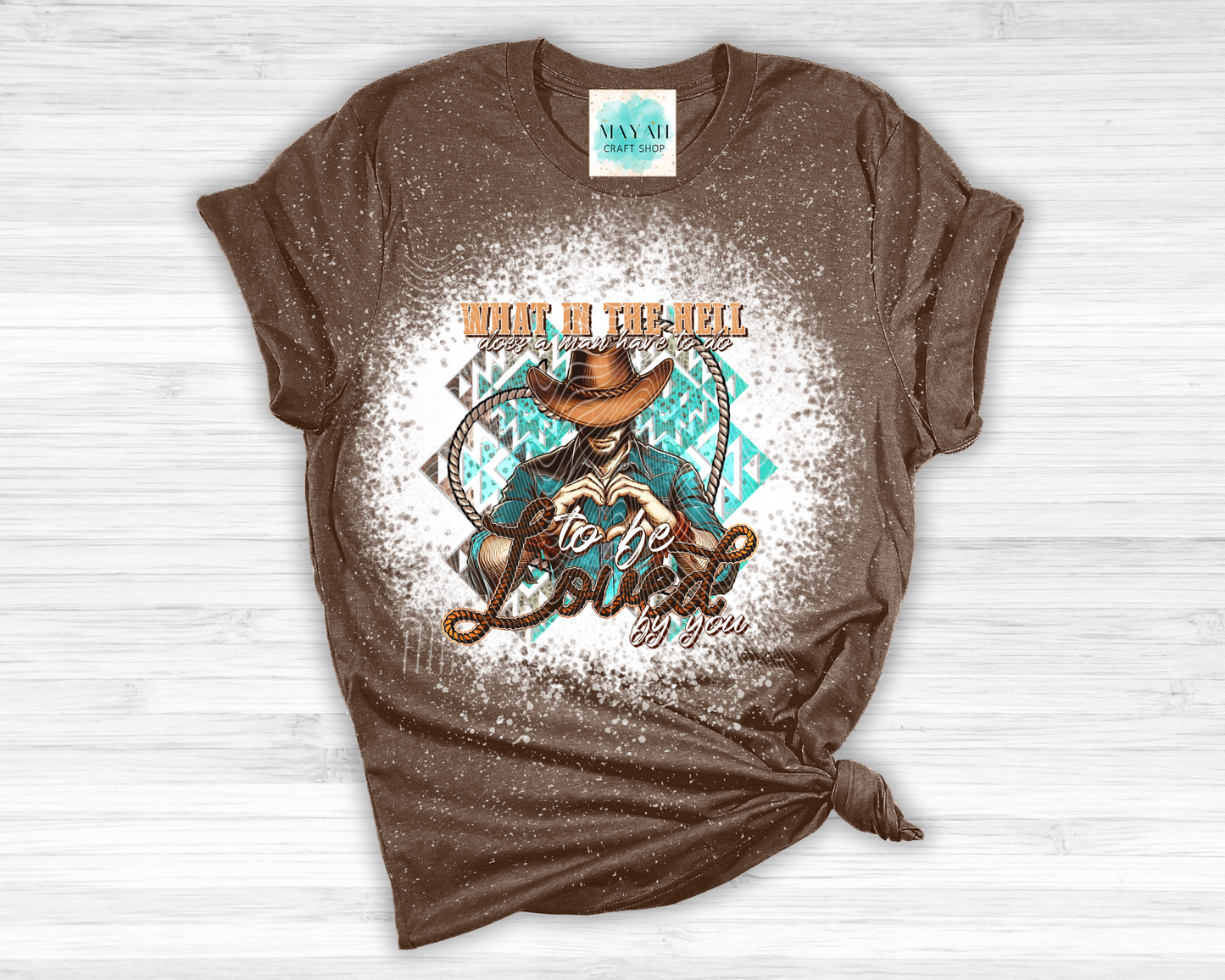 Brown t-shirt with graphic design and text on a white wooden surface