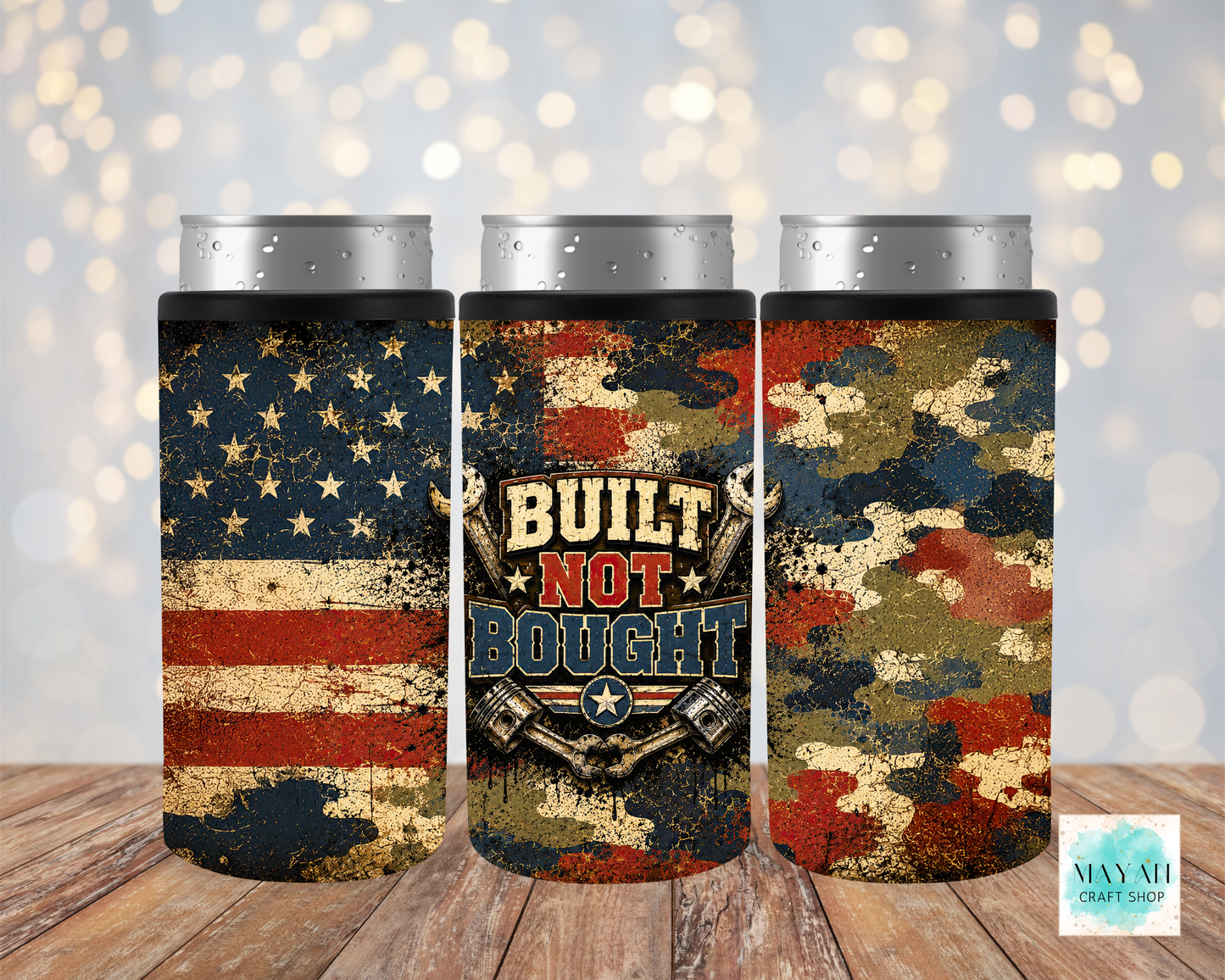 Three cylindrical can coolers with American flag, 'Built Not Bought' design, and camouflage patterns on a wooden surface.