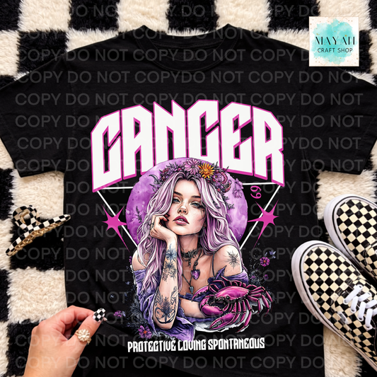 A black graphic t-shirt featuring a Cancer zodiac sign design with a purple-haired woman and a crab, styled flat-lay with checkered shoes and a checkered rug. A hand is holding a checkered accessory near the shirt.