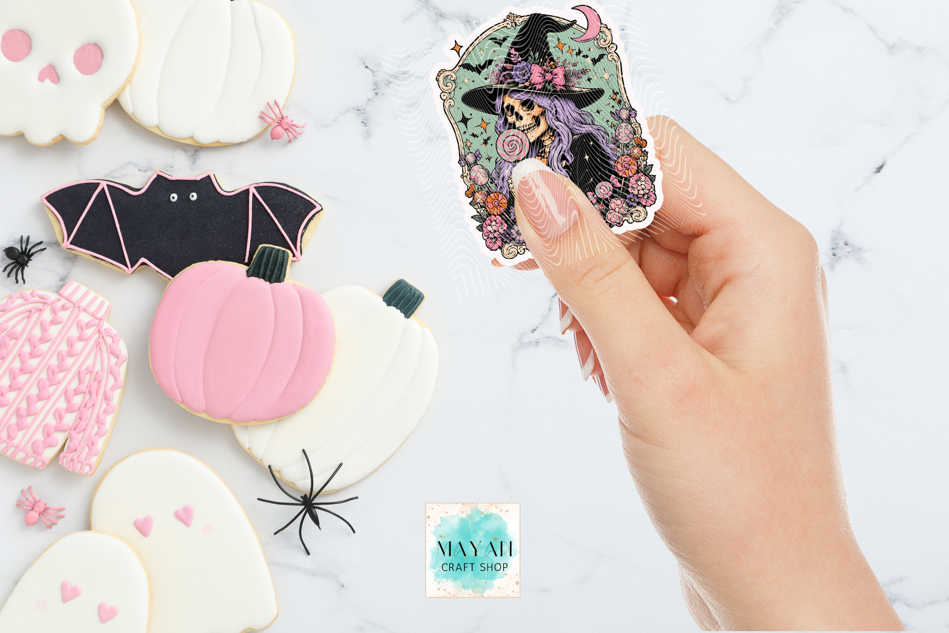 Hand holding a Halloween sticker with other decorated cookies on a marble surface.