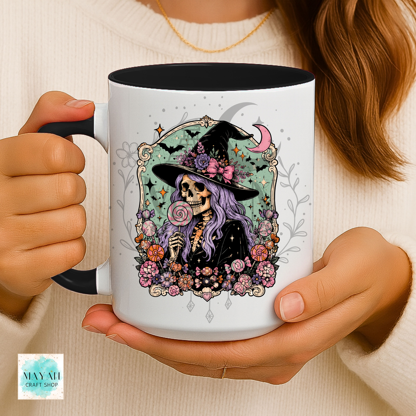Person holding a mug with a colorful skull and witch hat design.