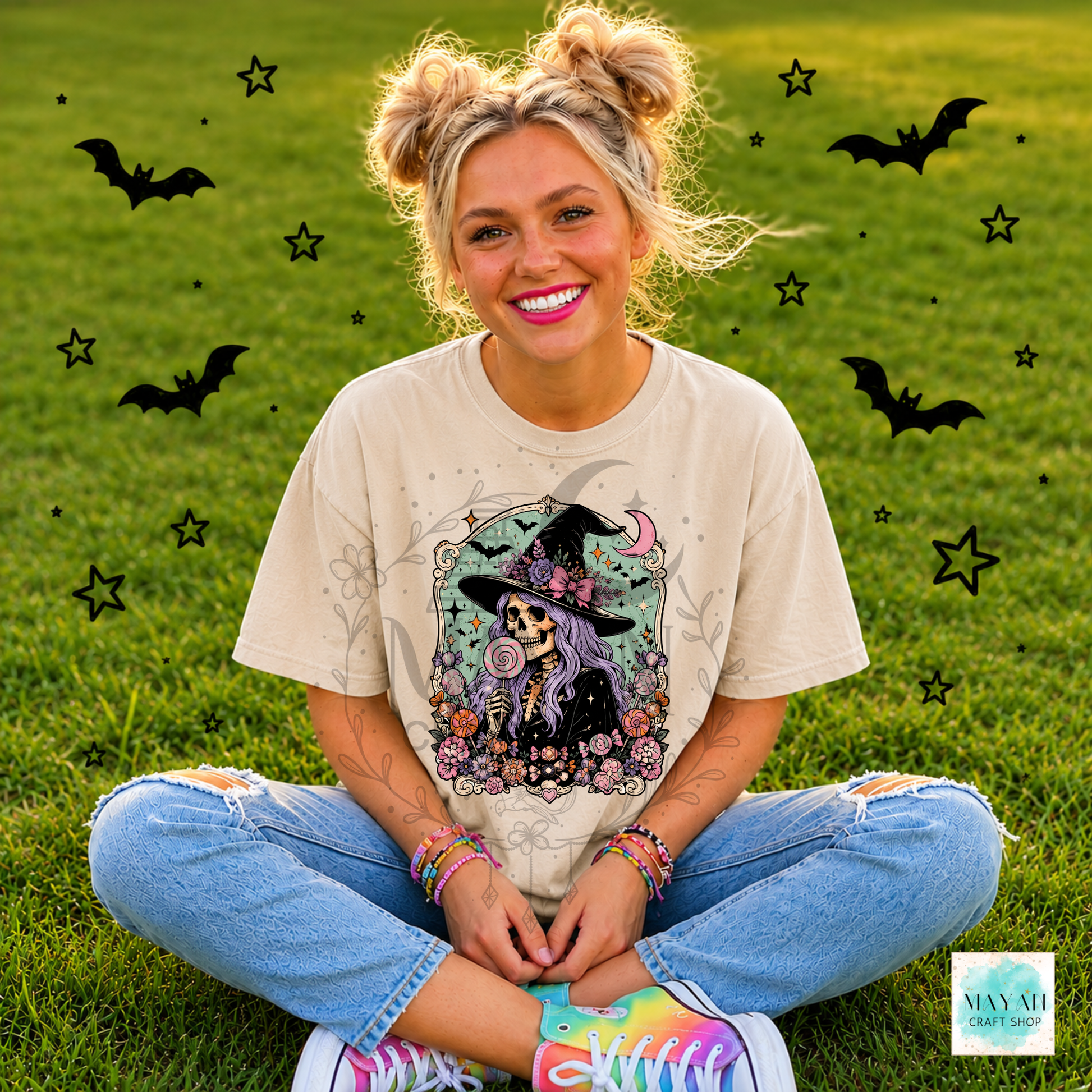 Person sitting on grass wearing a Halloween-themed t-shirt with decorative elements.
