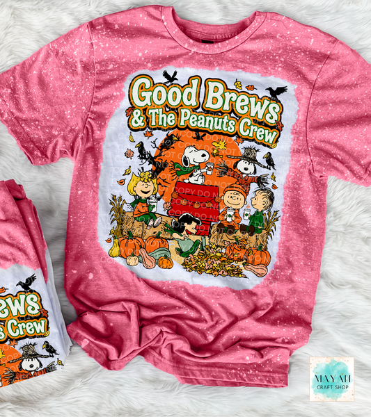 A heather cardinal bleached graphic t-shirt featuring 'Good Brews' with a colorful cartoon illustration of characters in an autumn setting. The shirt is laid flat on a white faux fur background, with a smaller folded duplicate of the shirt visible on the left.