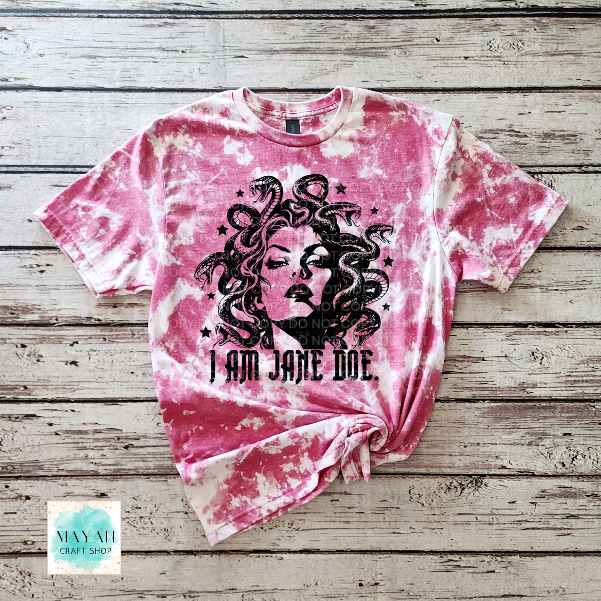 A heather cardinal red bleached graphic t-shirt featuring a black illustration of Medusa and the text 'I AM JANE DOE.' laid flat on a rustic wooden plank background.