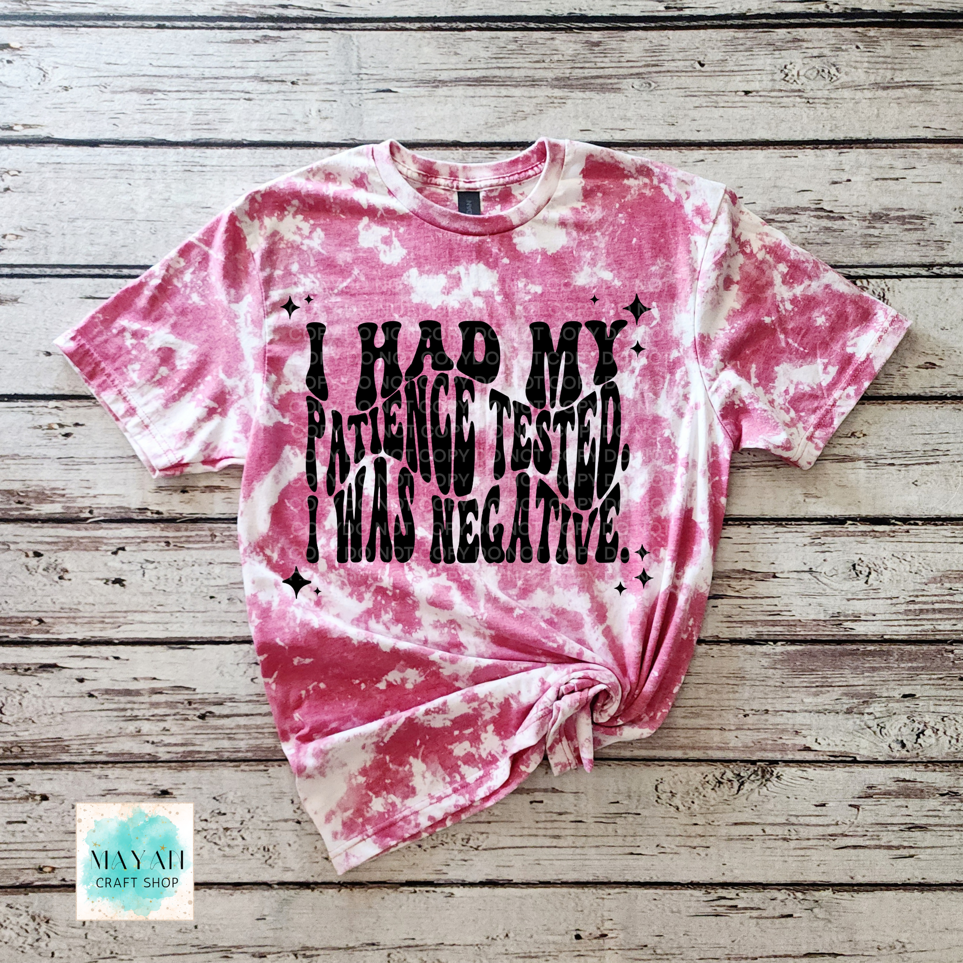 Pink tie-dye t-shirt with black text on a wooden surface, featuring the brand 'Mayan Craft Shop'.