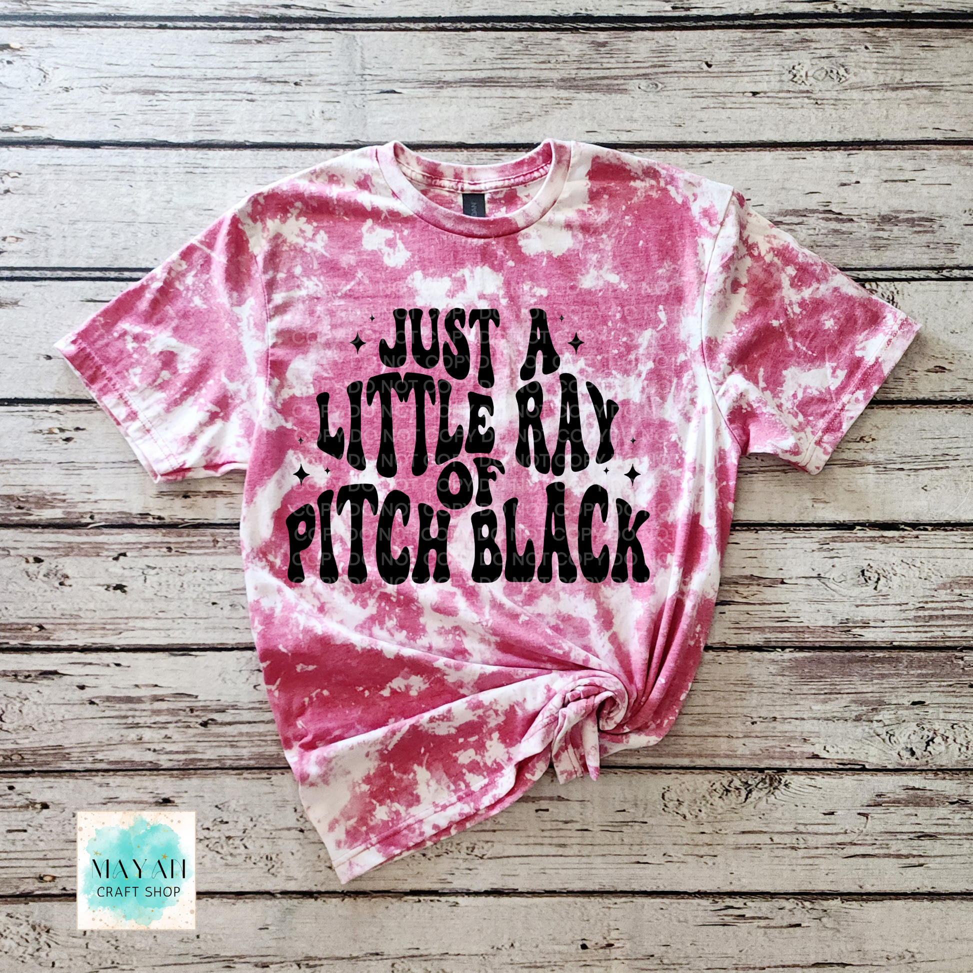 Pink tie-dye t-shirt with black text on a wooden surface, featuring the brand 'Mayan Craft Shop'.