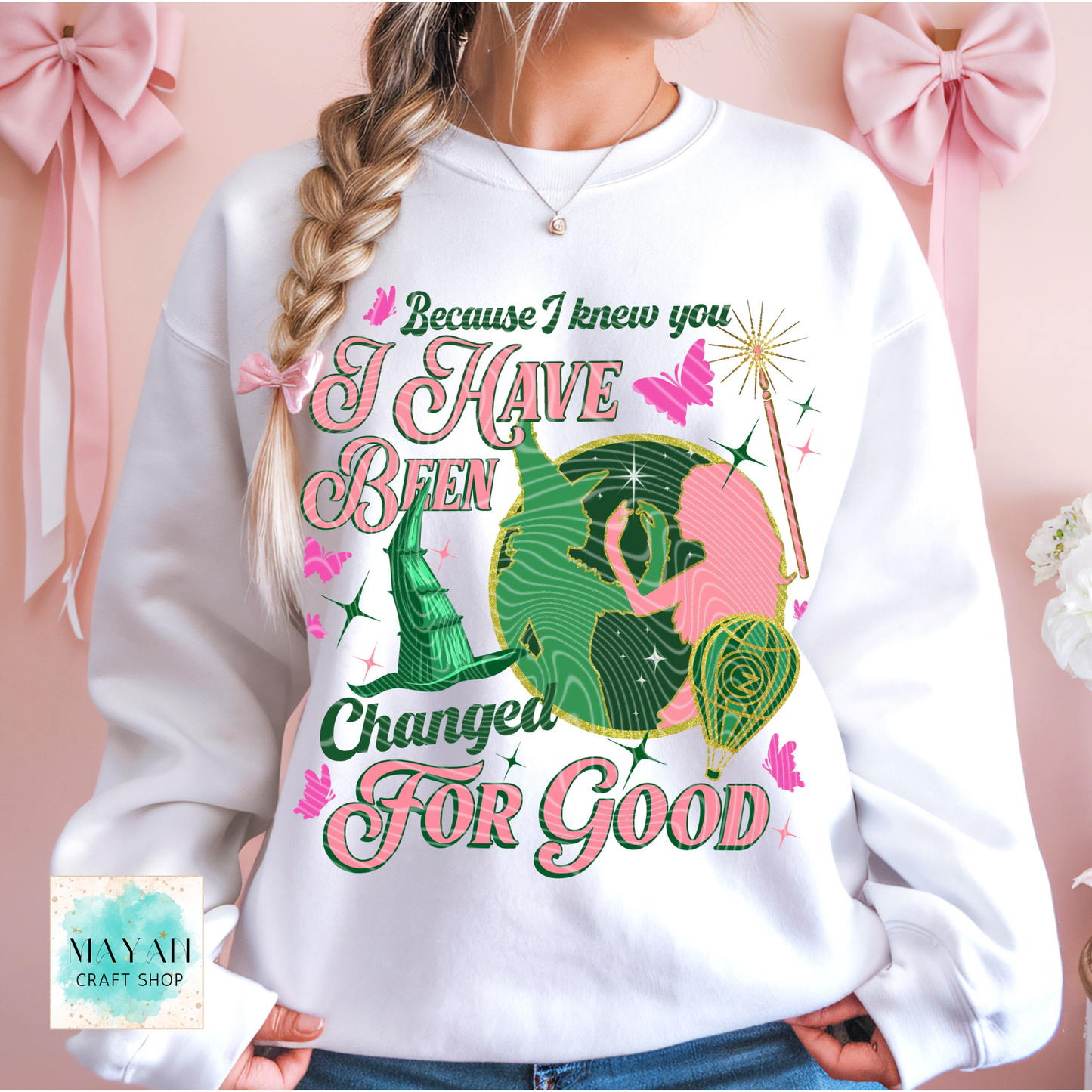 Person wearing a white sweatshirt with a colorful design and text, set against a pink background with bows.