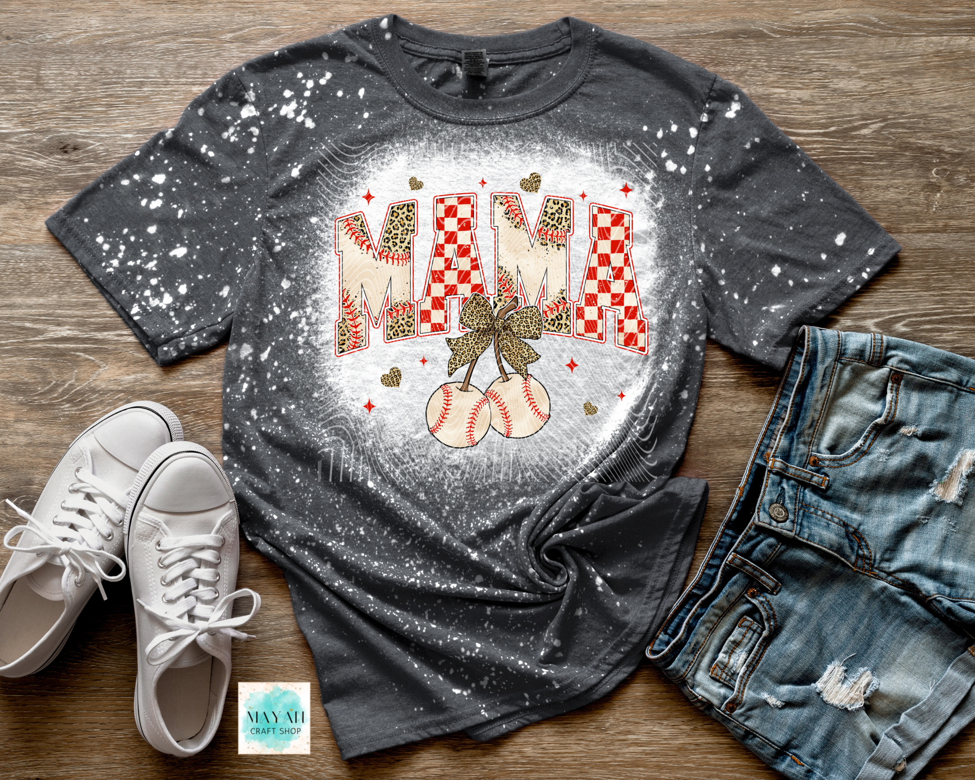 Gray t-shirt with 'MAMA' and cherry design on a wooden surface with white sneakers and jeans.