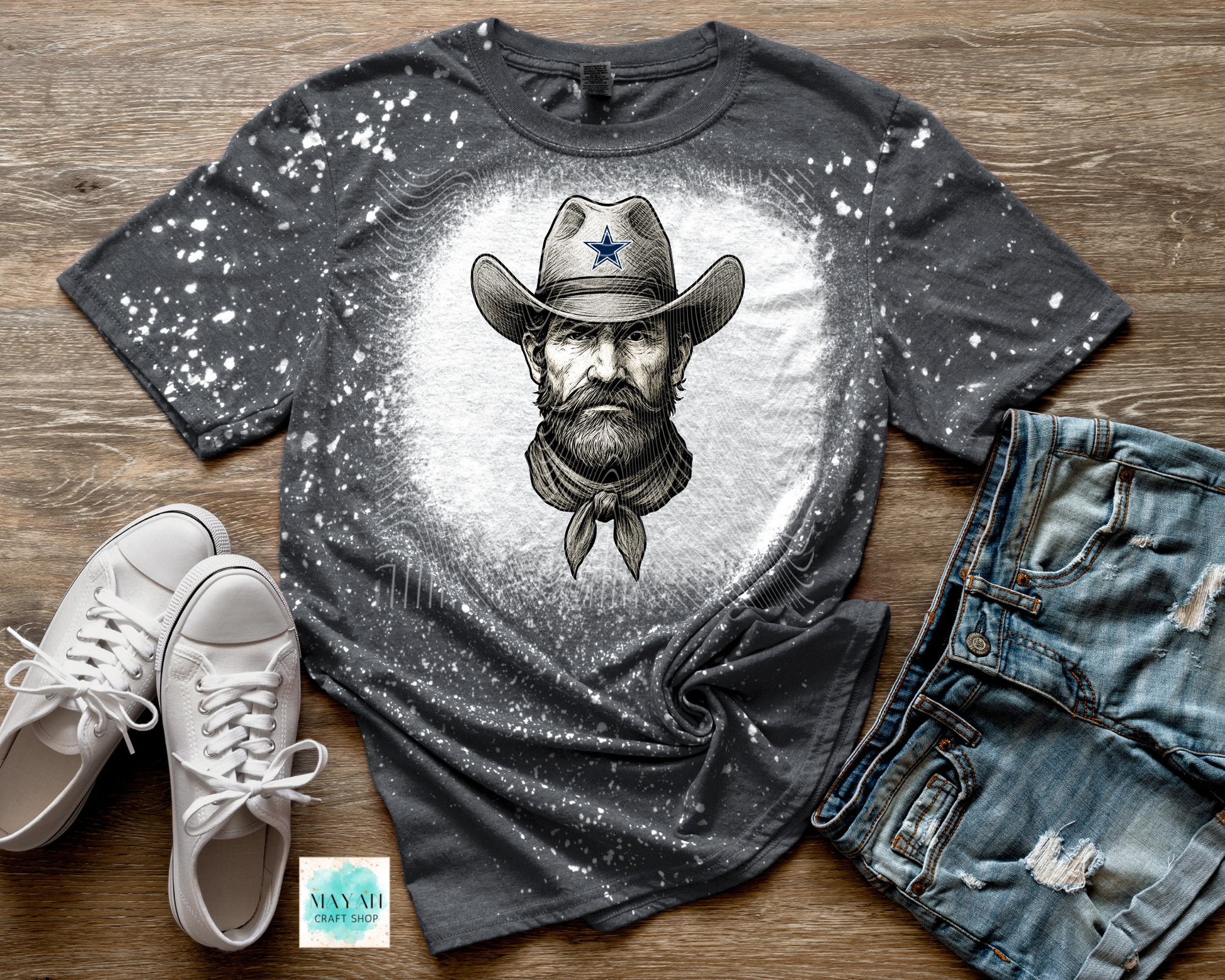 Gray t-shirt with cowboy graphic, white sneakers, and denim shorts on a wooden surface