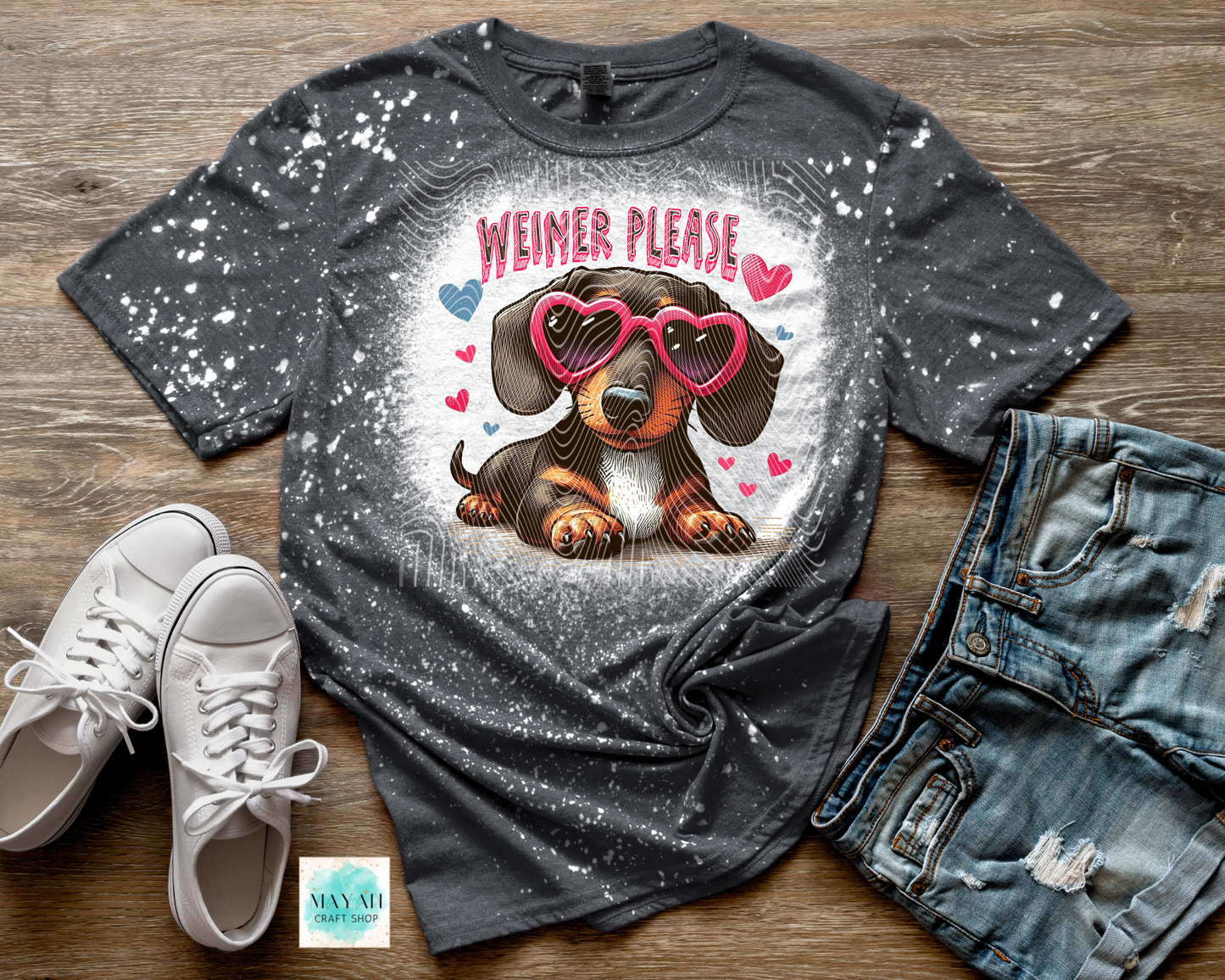 Gray t-shirt with a dog graphic and 'Weiner Please' text on a wooden surface with shoes and jeans.