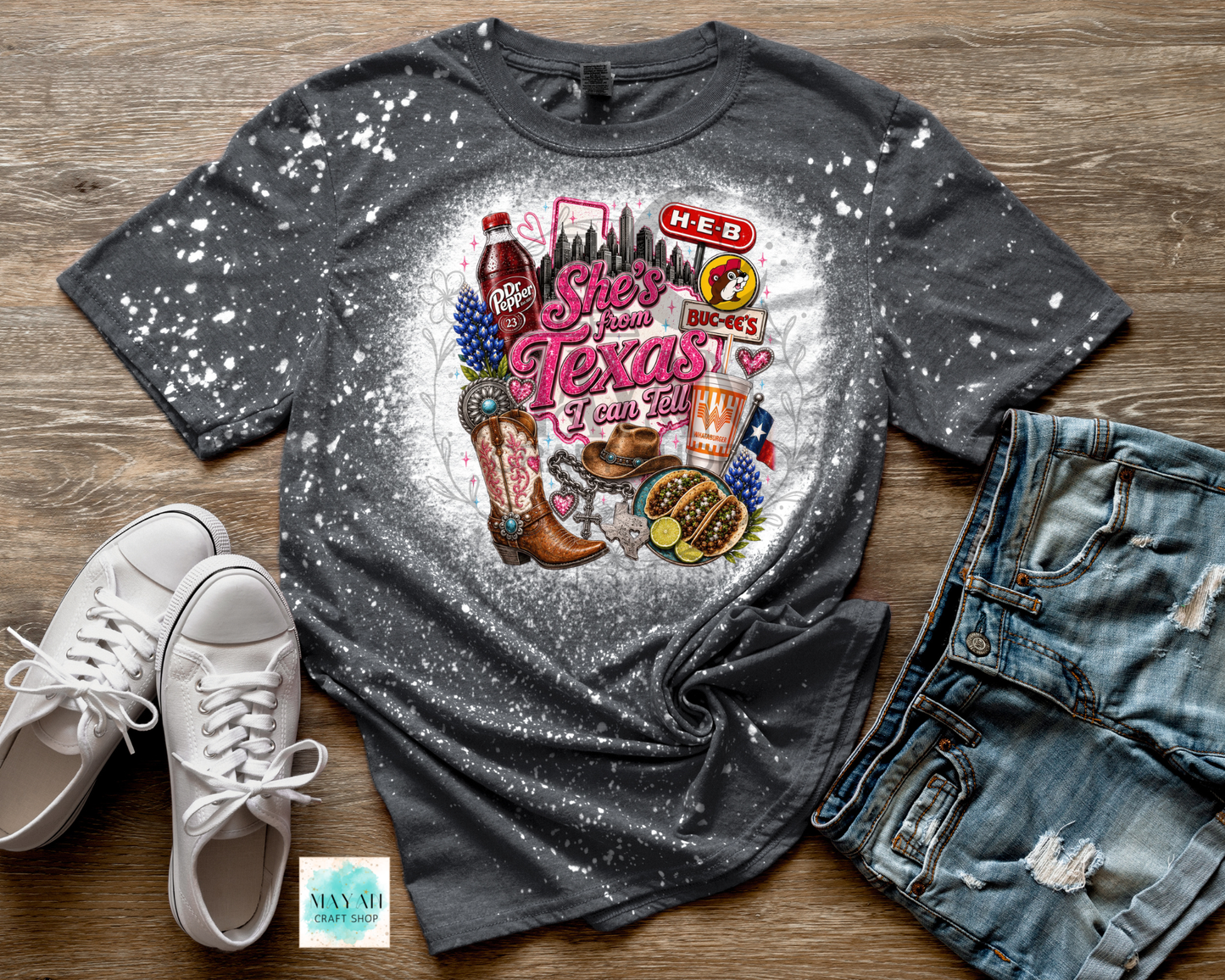 Gray t-shirt with Texas-themed graphic on a wooden surface with shoes and jeans.