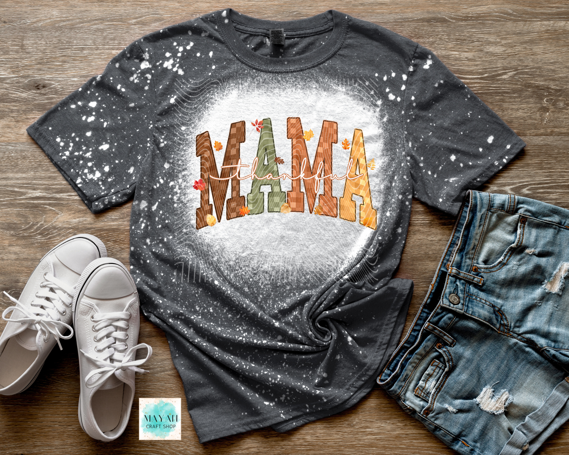 Gray t-shirt with 'MAMA' print on a wooden surface with sneakers and jeans.