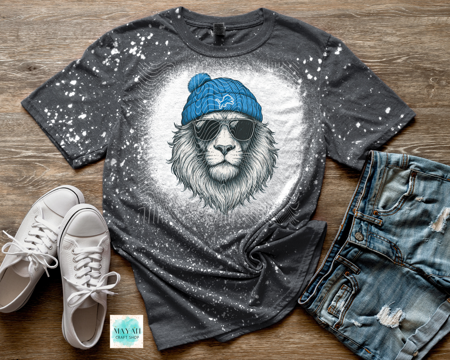 Gray t-shirt with lion graphic, blue beanie, sunglasses, white sneakers, and denim shorts on a wooden surface.