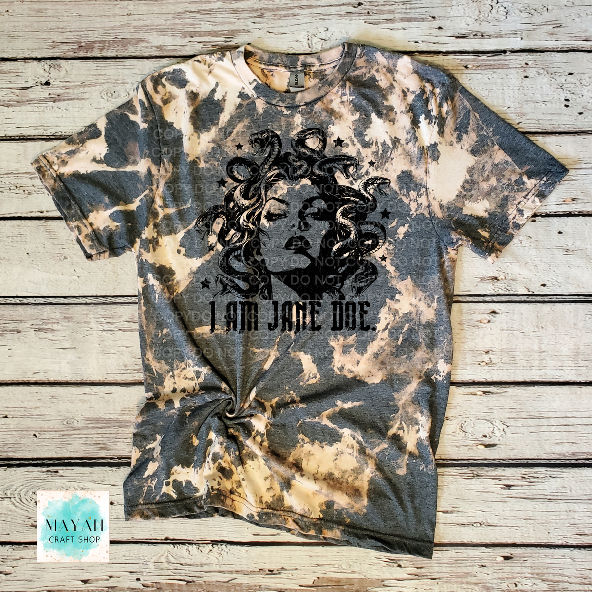 A short-sleeve crewneck heather charcoal bleached t-shirt, featuring a black graphic of Medusa's face with snakes for hair and the text 'I AM JANE DOE.' printed below.