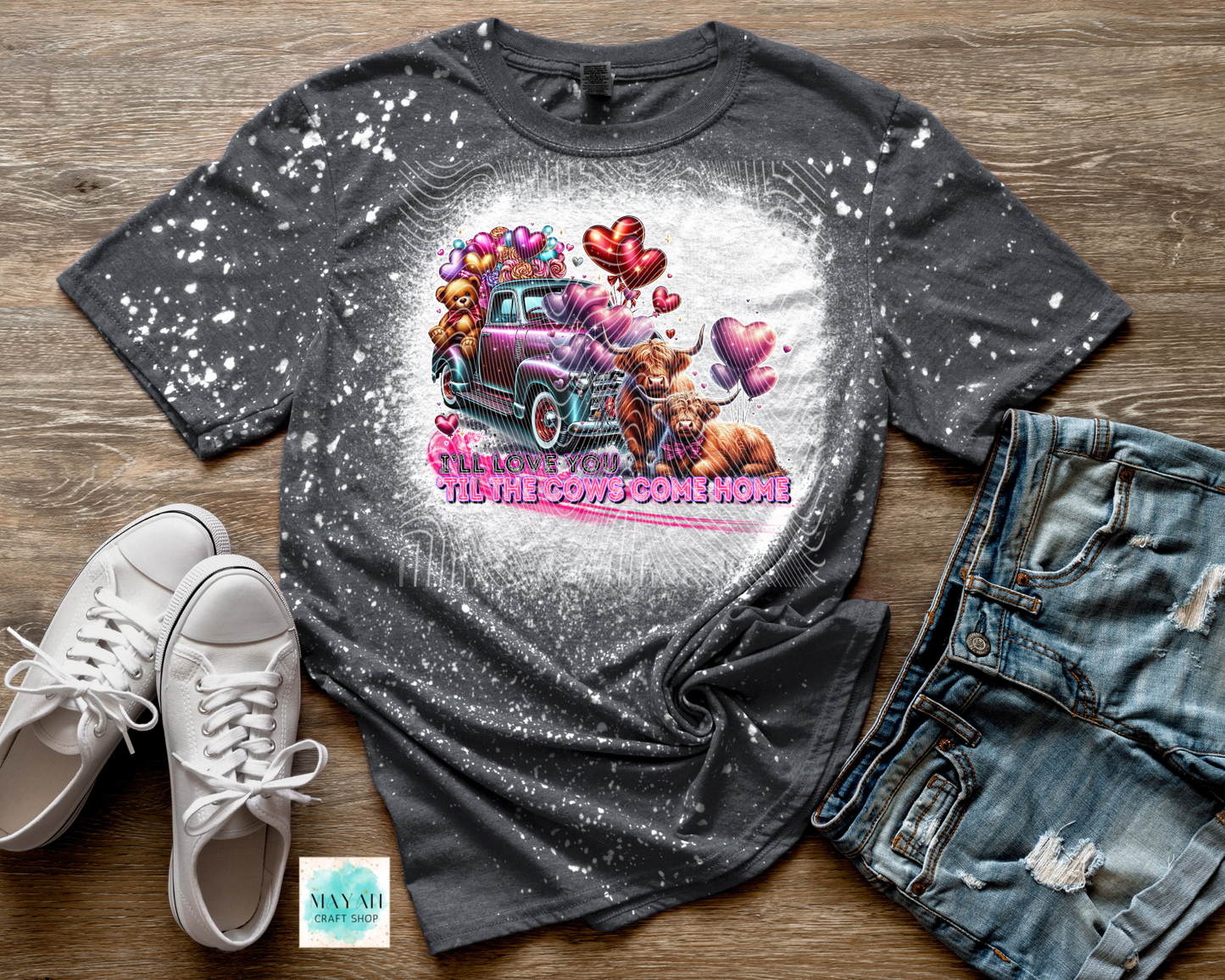 Gray t-shirt with a graphic design of a pink truck and teddy bears, paired with white sneakers and denim shorts on a wooden surface.